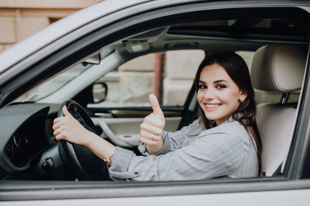 Beautiful young Latin woman driving her brand new car and showing her thumb up
